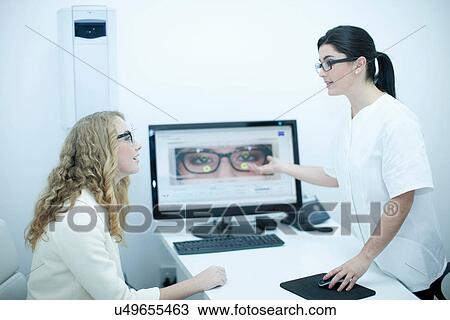 Stock Image - Optician guiding patient on choice of eyeglasses. Fotosearch