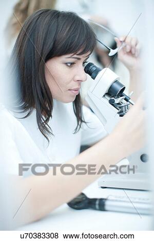 Optician looking through optical equipment View Large Photo Image Stock Photo - Optician looking through optical equipment. Fotosearch