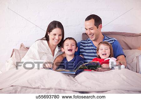 Parents and two young children looking at picture book in bed View Large Photo Image Stock Image - Parents and two young children looking at picture book in bed. Fotosearch