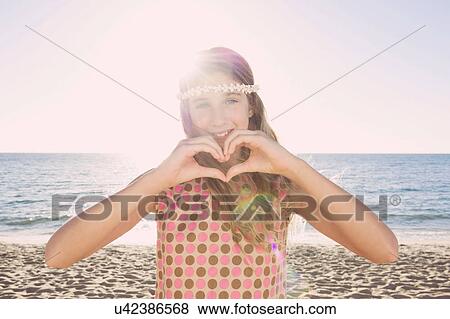 Stock Photo - Portrait of girl on beach making heart shape with hands. Fotosearch
