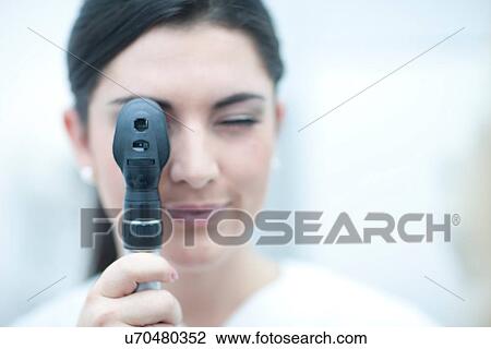 Stock Image - Portrait of optician looking through ophthalmoscope. Fotosearch