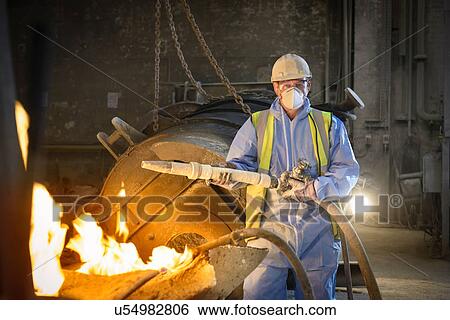 Stock Photograph - Portrait of steel worker holding industrial hose in steel foundry. Fotosearch