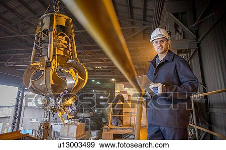 Stock Photo - Portrait of steel worker overseeing mechanical grabber in steel foundry. Fotosearch