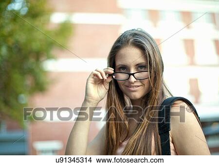 Picture - Portrait of young woman looking over her glasses on city street. Fotosearch
