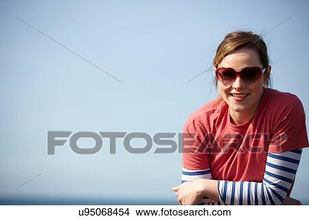 Portrait of young woman wearing heart shape sunglasses at coast View Large Photo Image Picture - Portrait of young woman wearing heart shape sunglasses at coast. Fotosearch