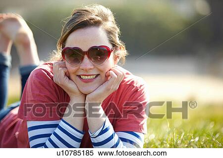 Portrait of young woman wearing heart shape sunglasses lying on grass View Large Photo Image Stock Photography - Portrait of young woman wearing heart shape sunglasses lying on grass. Fotosearch