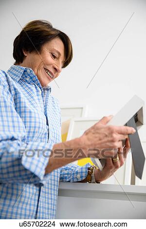 Picture - Senior woman looking at picture frame. Fotosearch