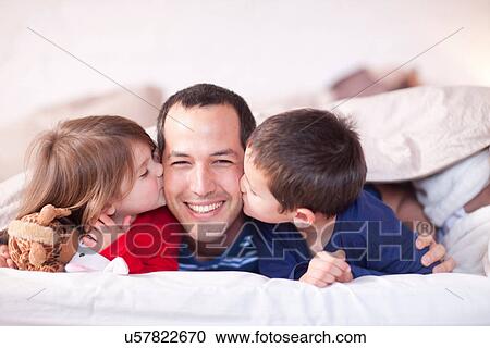 Son and daughter kissing fathers cheek under duvet View Large Photo Image Stock Image - Son and daughter kissing fathers cheek under duvet. Fotosearch