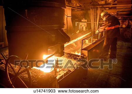 Stock Image - Steel worker attending furnace in steel foundry. Fotosearch