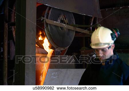Stock Image - Steel worker in front of running molten metal in steel foundry. Fotosearch