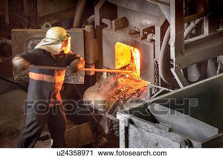 Stock Image - Steel worker poking furnace in steel foundry. Fotosearch