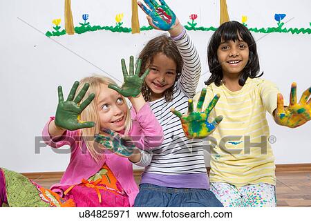 Stock Image - Three girls kneeling on floor with painted hands. Fotosearch