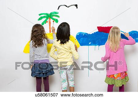 Stock Photo - Three girls painting ocean and island on wall. Fotosearch