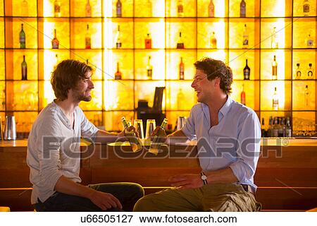 Stock Photo - Two men sitting at bar with bottles of beer. Fotosearch