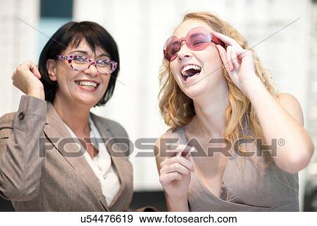 Two women laughing whilst trying on eyeglasses View Large Photo Image Stock Photo - Two women laughing whilst trying on eyeglasses. Fotosearch