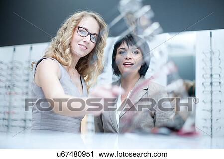 Two women looking at eyeglasses in opticians shop View Large Photo Image Stock Image - Two women looking at eyeglasses in opticians shop. Fotosearch