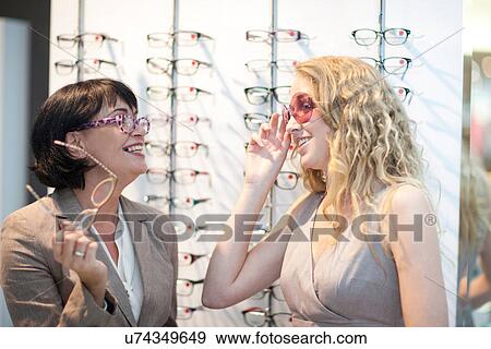 Two women trying on eyeglasses in opticians shop View Large Photo Image Stock Photo - Two women trying on eyeglasses in opticians shop. Fotosearch
