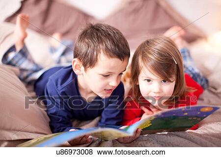 Stock Photo - Two young children lying on bed looking at picture book. Fotosearch
