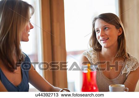 Stock Image - Two young women chatting in cafe bar. Fotosearch