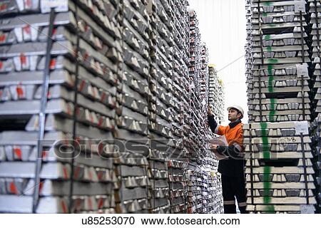 Stock Image - Warehouse worker checking stacked aluminum ingots. Fotosearch