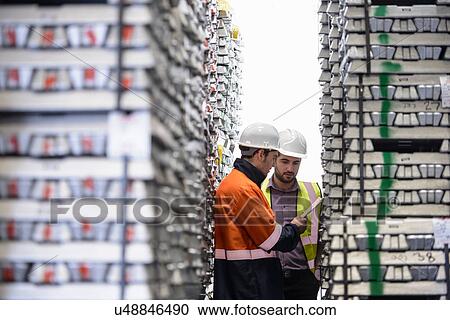 Stock Image - Warehouse workers checking stacked aluminum ingots. Fotosearch