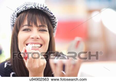 Stock Image - Woman in checked cap applying lipstick. Fotosearch
