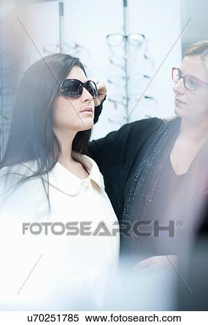 Stock Photography - Woman trying on sunglasses in opticians shop. Fotosearch