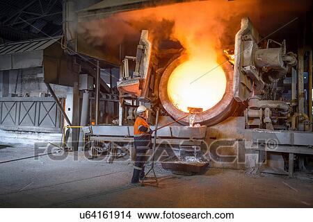 Picture - Worker raking liquid aluminum from furnace at recycling plant. Fotosearch