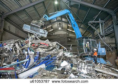 Workers and excavator lifting scrap metal in warehouse View Large Photo Image Stock Photo - Workers and excavator lifting scrap metal in warehouse. Fotosearch