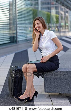 Stock Photo - Young businesswoman sitting and using mobile phone, smiling. Fotosearch