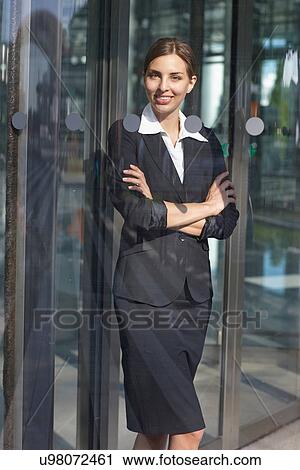 Stock Image - Young businesswoman standing in glass doorway. Fotosearch