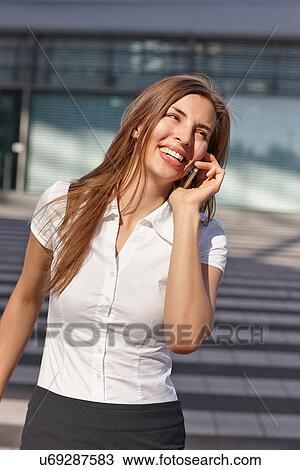 Stock Image - Young businesswoman using mobile phone, smiling. Fotosearch