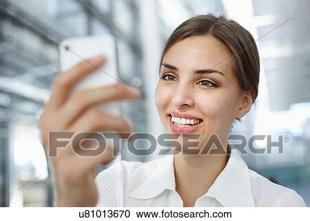 Stock Image - Young businesswoman using mobile phone, smiling. Fotosearch