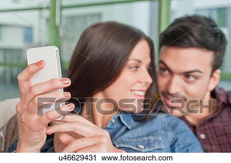Young couple at home looking at mobile phone View Large Photo Image Stock Image - Young couple at home looking at mobile phone. Fotosearch