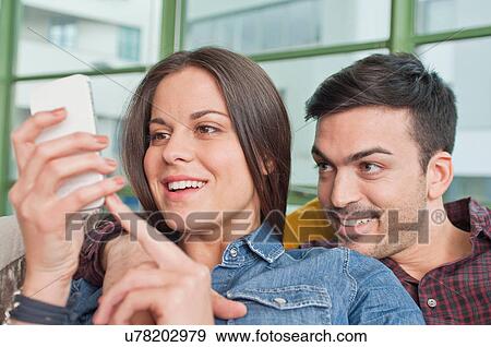 Stock Photo - Young couple at home sharing mobile phone. Fotosearch