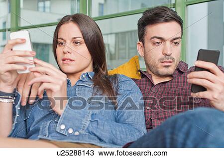 Young couple at home using mobile phones View Large Photo Image Stock Image - Young couple at home using mobile phones. Fotosearch