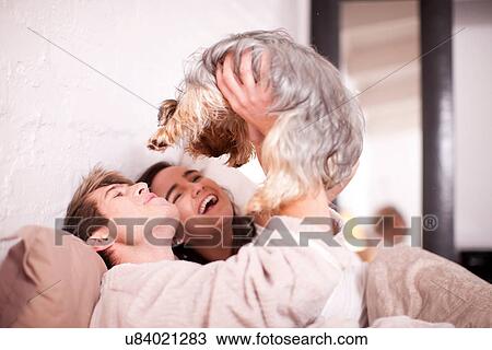 Young couple in bed with pet dog View Large Photo Image Stock Image - Young couple in bed with pet dog. Fotosearch