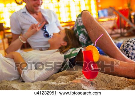 Stock Image - Young couple lounging on sand at indoor beach party. Fotosearch