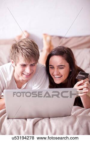 Young couple lying on bed looking at laptop View Large Photo Image Stock Photo - Young couple lying on bed looking at laptop. Fotosearch