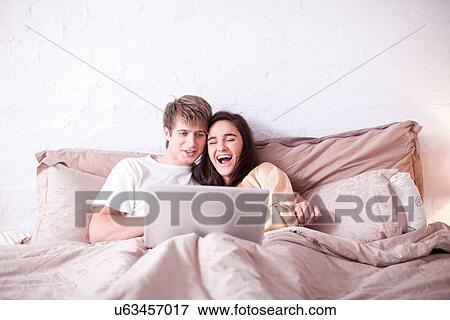 Young couple watching laptop in bed View Large Photo Image Stock Photo - Young couple watching laptop in bed. Fotosearch