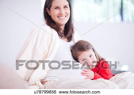 Stock Photograph - Young daughter hugging mothers bump on bed. Fotosearch