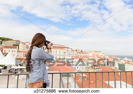 Stock Photograph - Young female tourist photographing in Alfama District, Lisbon, Portugal. Fotosearch