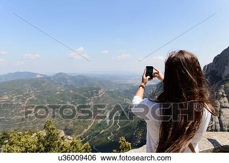 Stock Photograph - Young female tourist photographing the view of montserrat, Spain. Fotosearch