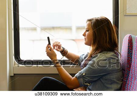 Young female using smartphone whilst on train View Large Photo Image Stock Photo - Young female using smartphone whilst on train. Fotosearch