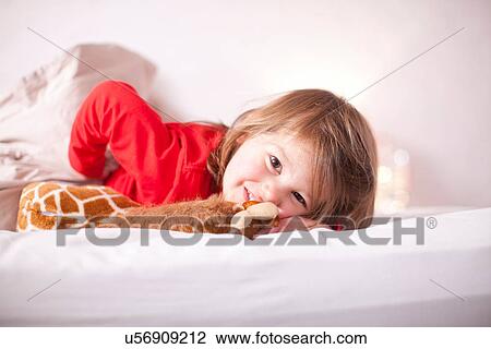 Stock Image - Young girl lying on bed with toy giraffe. Fotosearch