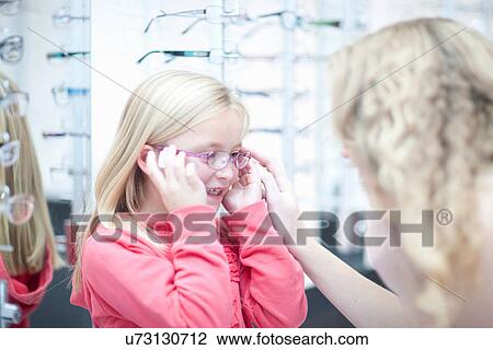 Stock Image - Young girl trying on eyeglasses. Fotosearch