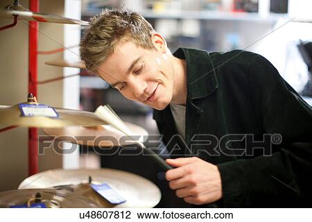 Stock Image - Young male trying drum kit in music store. Fotosearch