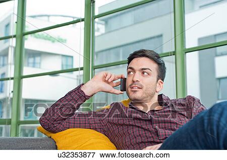 Young man at home using his mobile phone View Large Photo Image Stock Photo - Young man at home using his mobile phone. Fotosearch