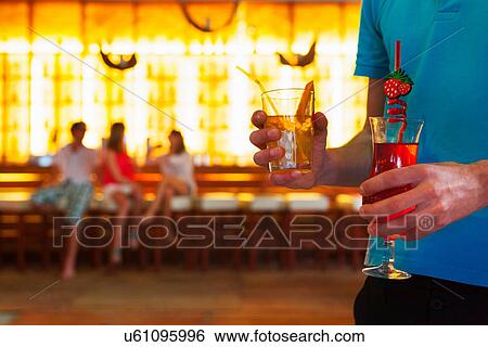 Stock Photograph - Young man carrying cocktails in bar. Fotosearch