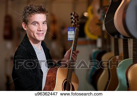 Young man looking at guitars in music store View Large Photo Image Stock Photo - Young man looking at guitars in music store. Fotosearch